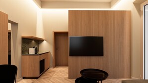 Ein modernes Hotelzimmer mit Holzboden, einem flachbildfernseher an der Wand, einem kleinen Tisch und einem Stuhl.