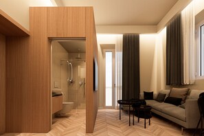 Ein modernes Hotelzimmer mit einem Holzschrank, einer Duschkabine aus Glas, einem Sofa und einem Couchtisch.