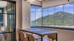 Une pièce avec une table et des chaises, une fenêtre donnant sur une plage et des montagnes, et un rideau.