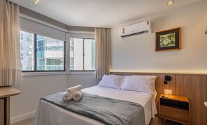 A hotel room with a bed, a bedside table, an air conditioning unit, a window with curtains, and a framed picture on the wall. - Apt With 2 Suites Beachfront in BC Eqc0801 (Balneário Camboriú)