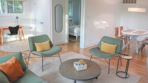 A modern living room with a round coffee table, two green armchairs with yellow cushions, a sofa with an orange cushion, and a dining area with a white table and chairs. - The Private Oasis • 22 min to downtown (Indianapolis)