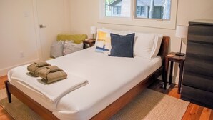 A bedroom with a wooden bed, white linens, a window with a view of a house, a bedside table with a lamp, and a dark dresser. - The Private Oasis • 22 min to downtown (Indianapolis)