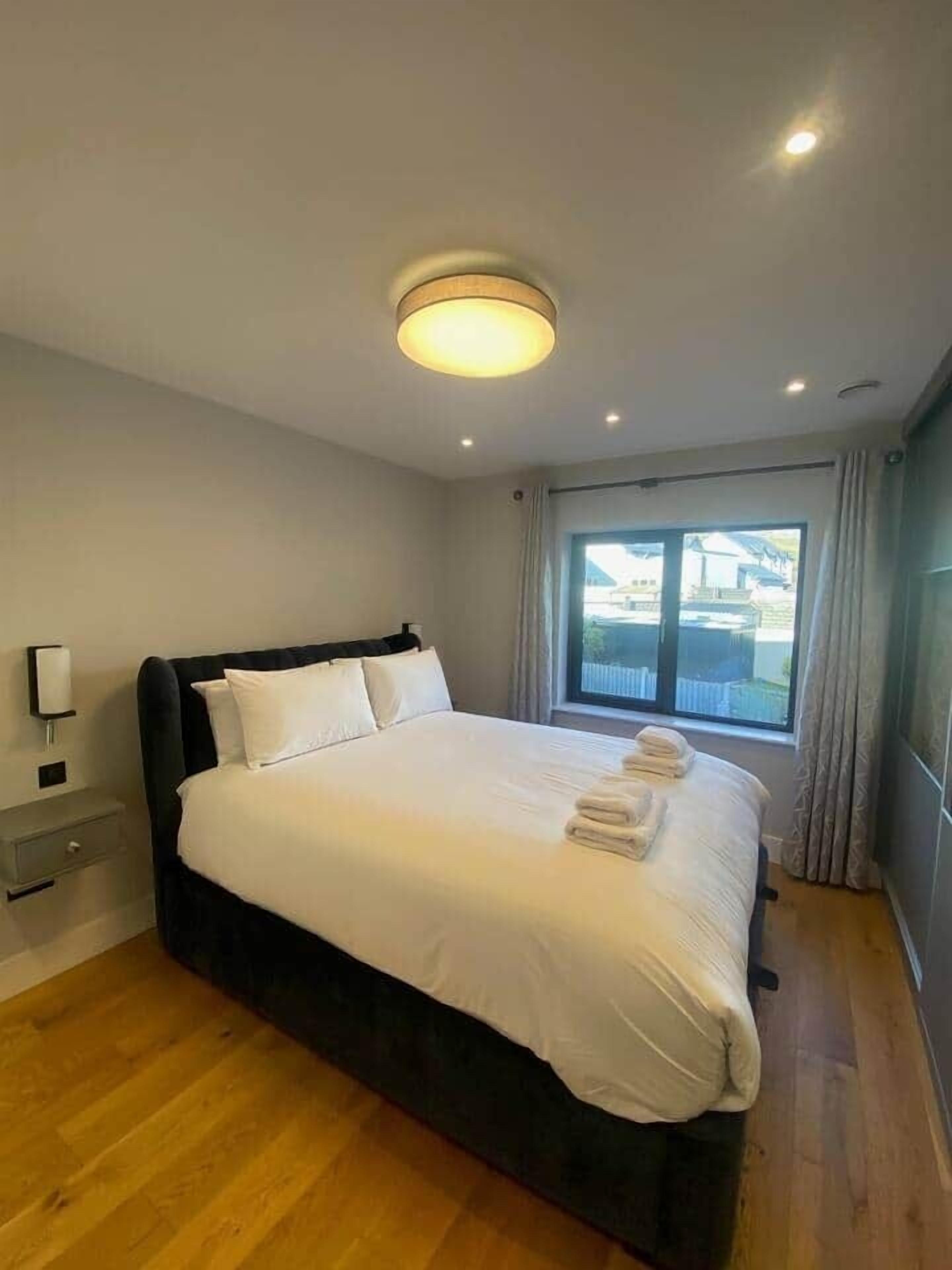 A modern hotel room with a large bed, a bedside table, a nightstand, and a window with curtains.