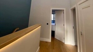 A modern hallway with a wooden floor, white walls, and a blue accent wall. There are pendant lights hanging from the ceiling and a wooden railing with integrated lighting. - Dingle Doorstep - Town Centre (Dingle)