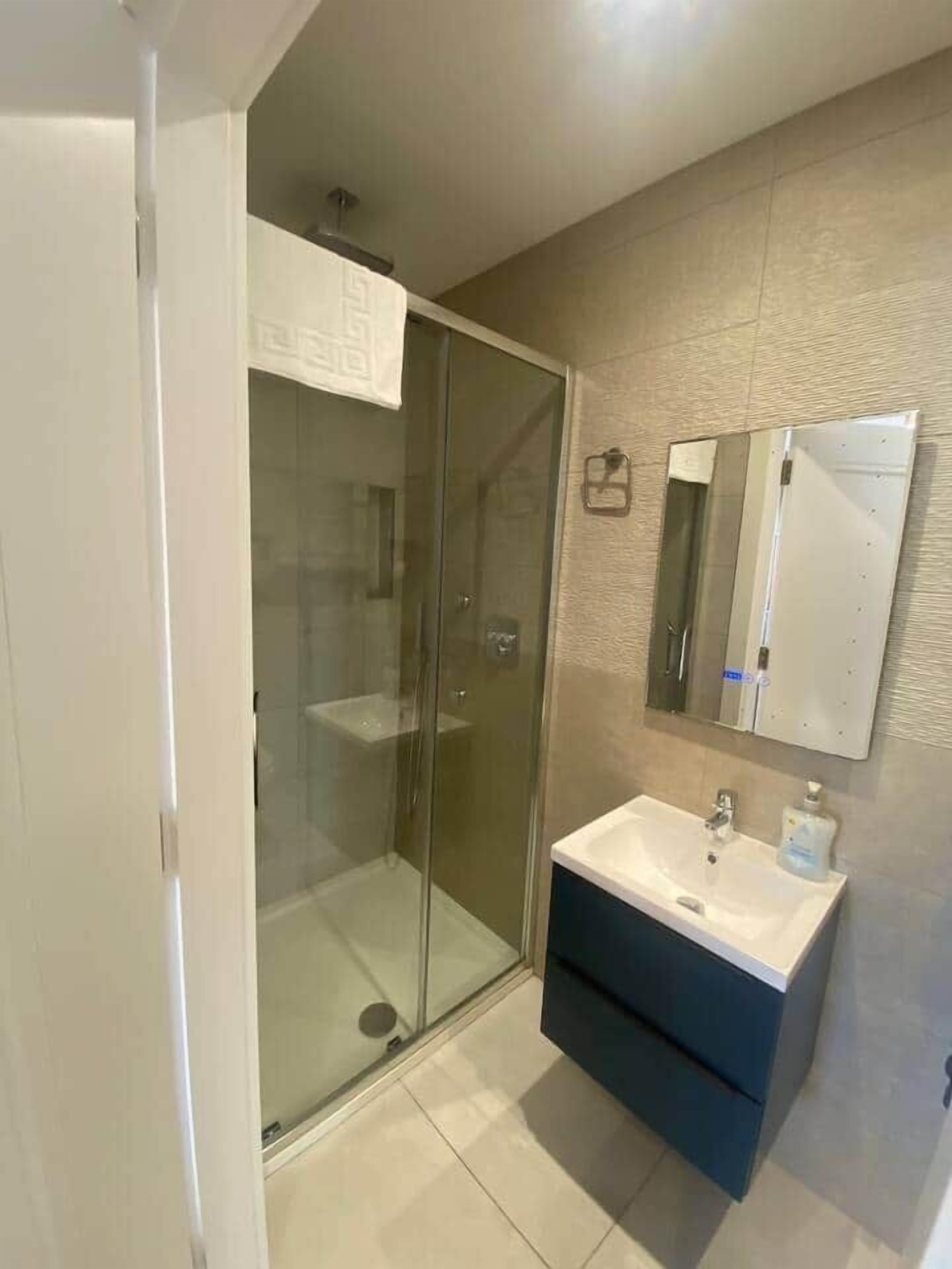 Een moderne badkamer met een douchecabine van glas, een wastafel met spiegel erboven en een donker kastje eronder.