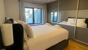 A modern hotel room with a large bed, a bedside table, a mirror, and a window with curtains. - Dingle Doorstep - Town Centre (Dingle)