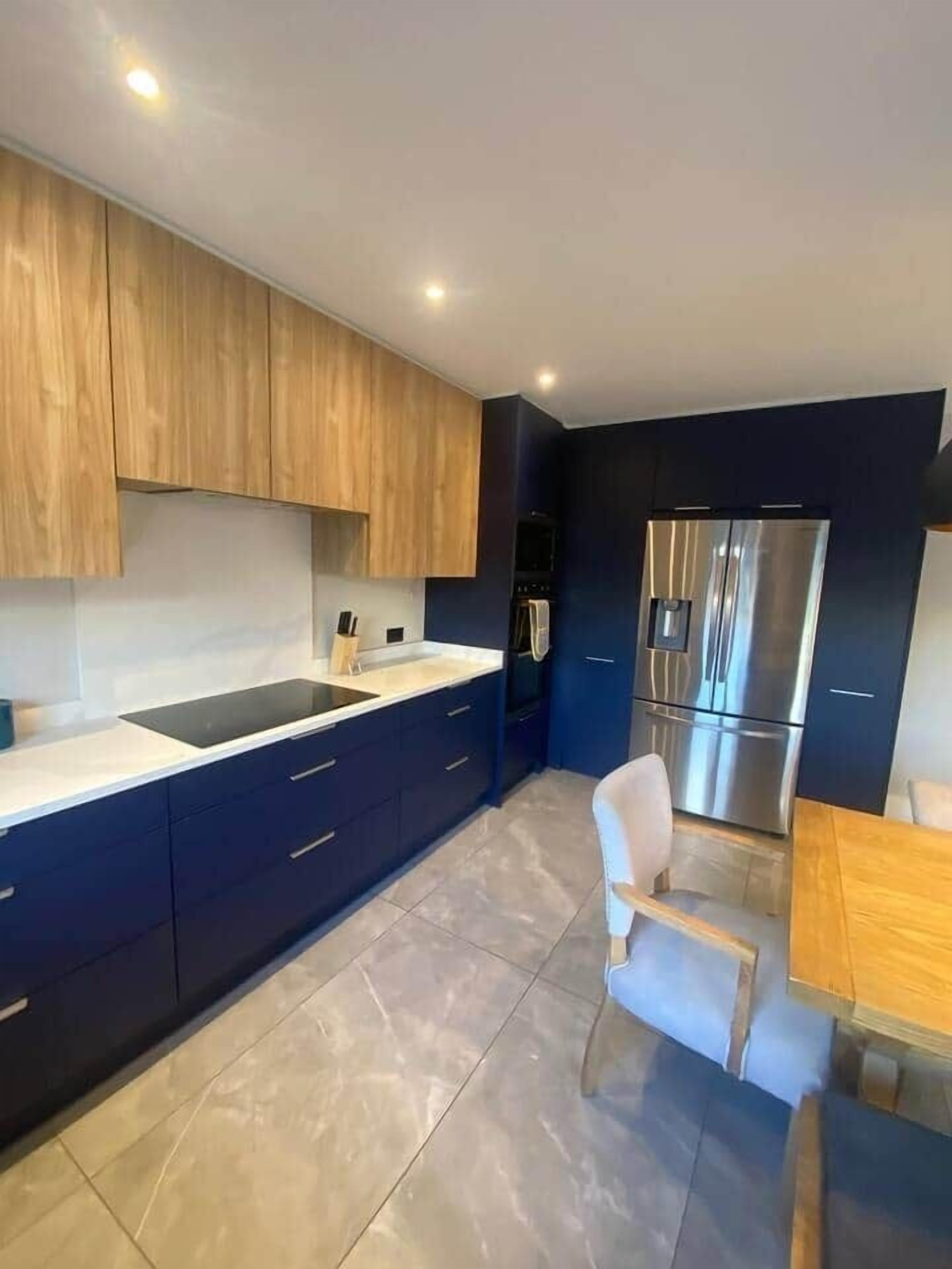 A modern kitchen with dark blue cabinets, a stainless steel refrigerator, and a white countertop.