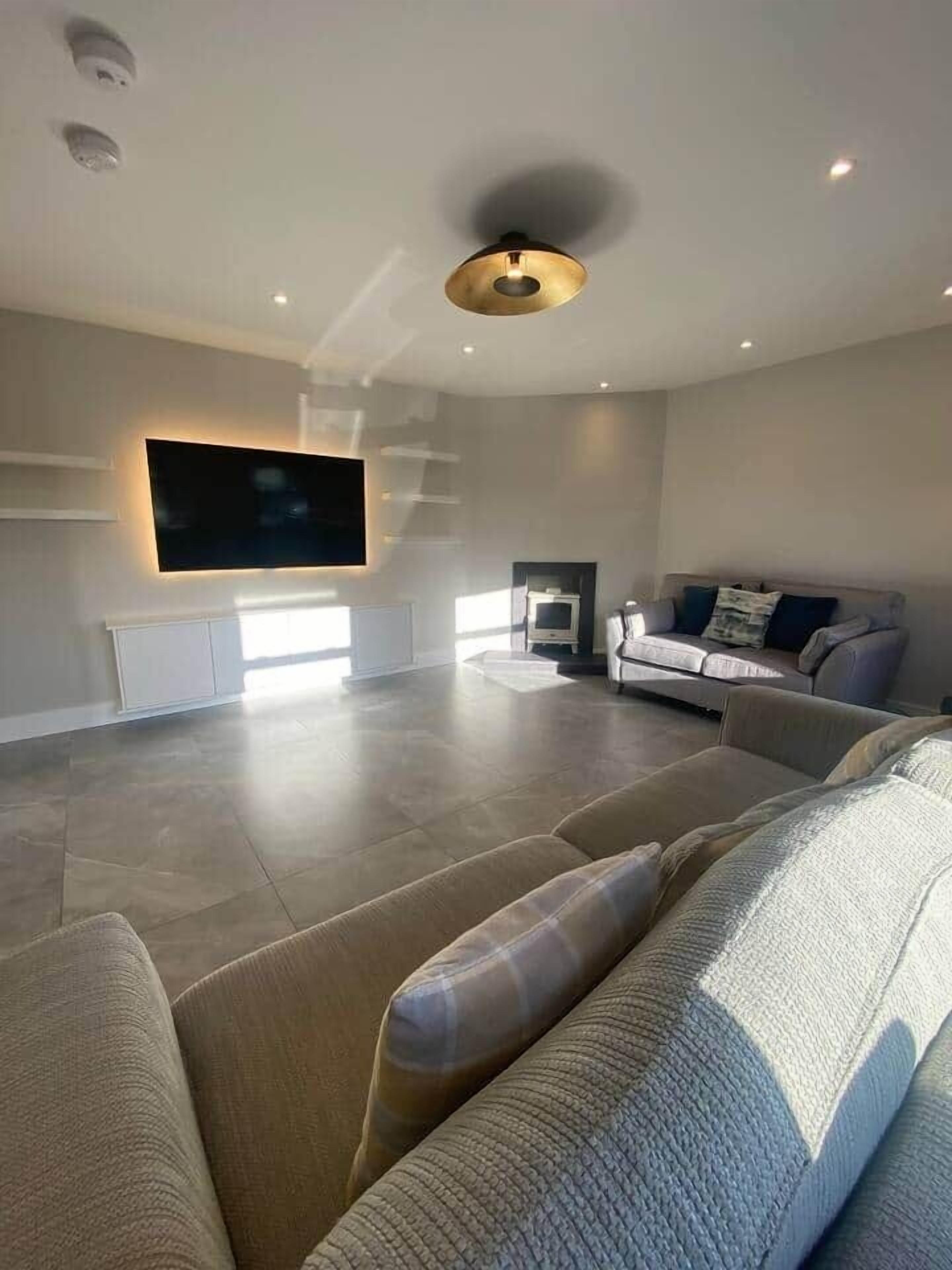 A modern living room with a large flat-screen TV mounted on the wall, a sofa, and a fireplace.