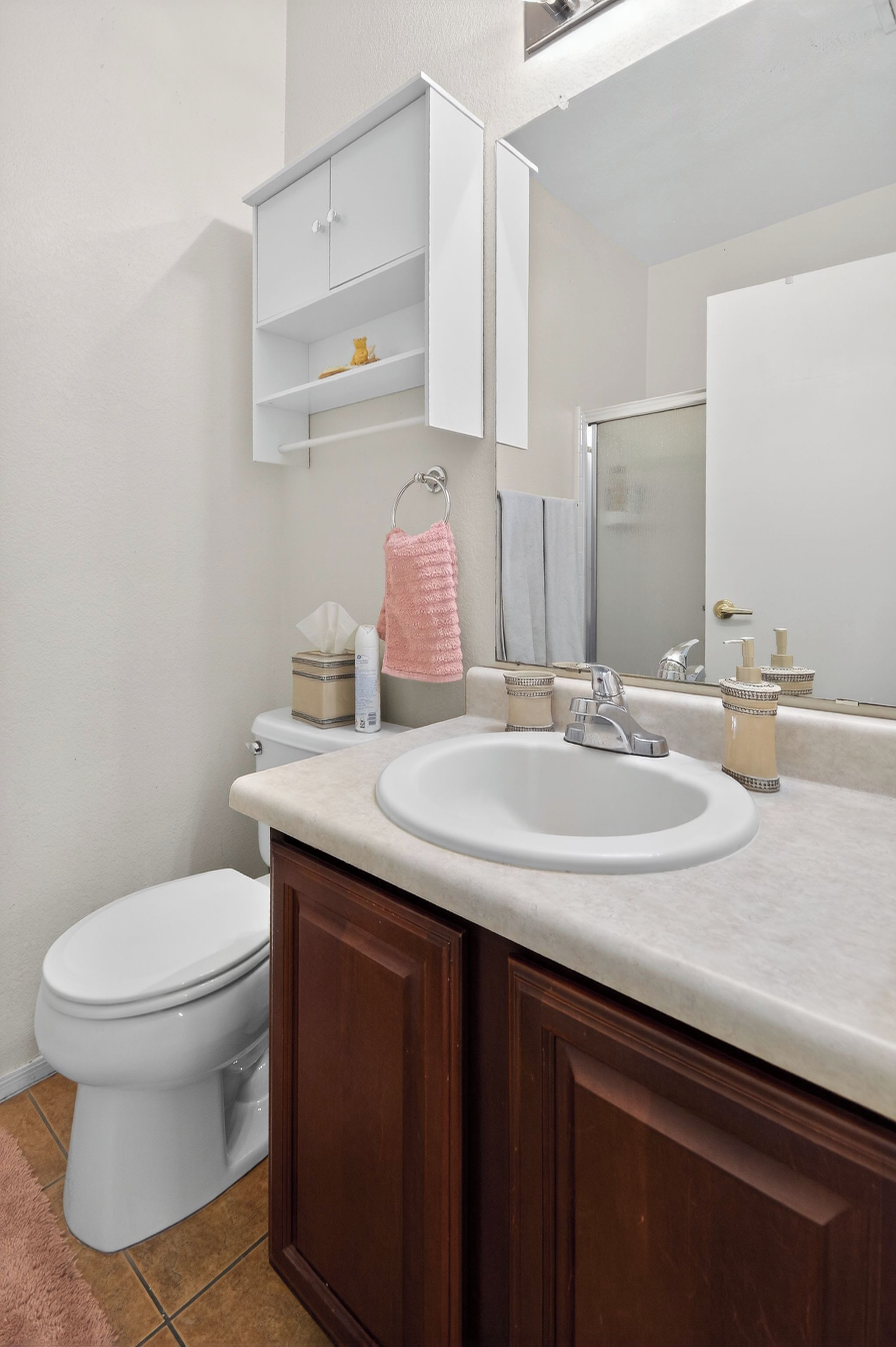 A bathroom with a white sink, a mirror, a toilet, and a cabinet with toiletries.
