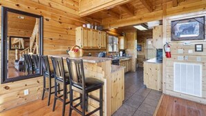 Interior de cabana de madeira com sala de jantar, cozinha e uma grande janela.