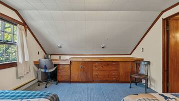 A bedroom with a sloped ceiling, a desk, a chair, a wardrobe, and two beds.