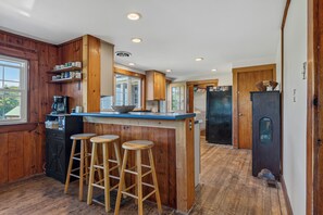 A kitchen with wooden cabinets, a bar area with stools, and a refrigerator.