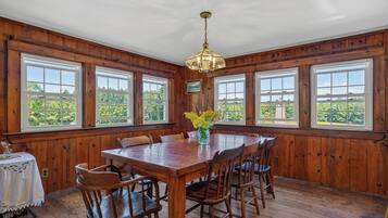 A dining room with a wooden table and chairs, large windows, and a chandelier.