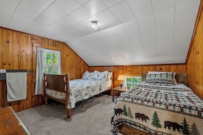 A bedroom with two beds, wooden walls, a ceiling light, and a window with curtains.