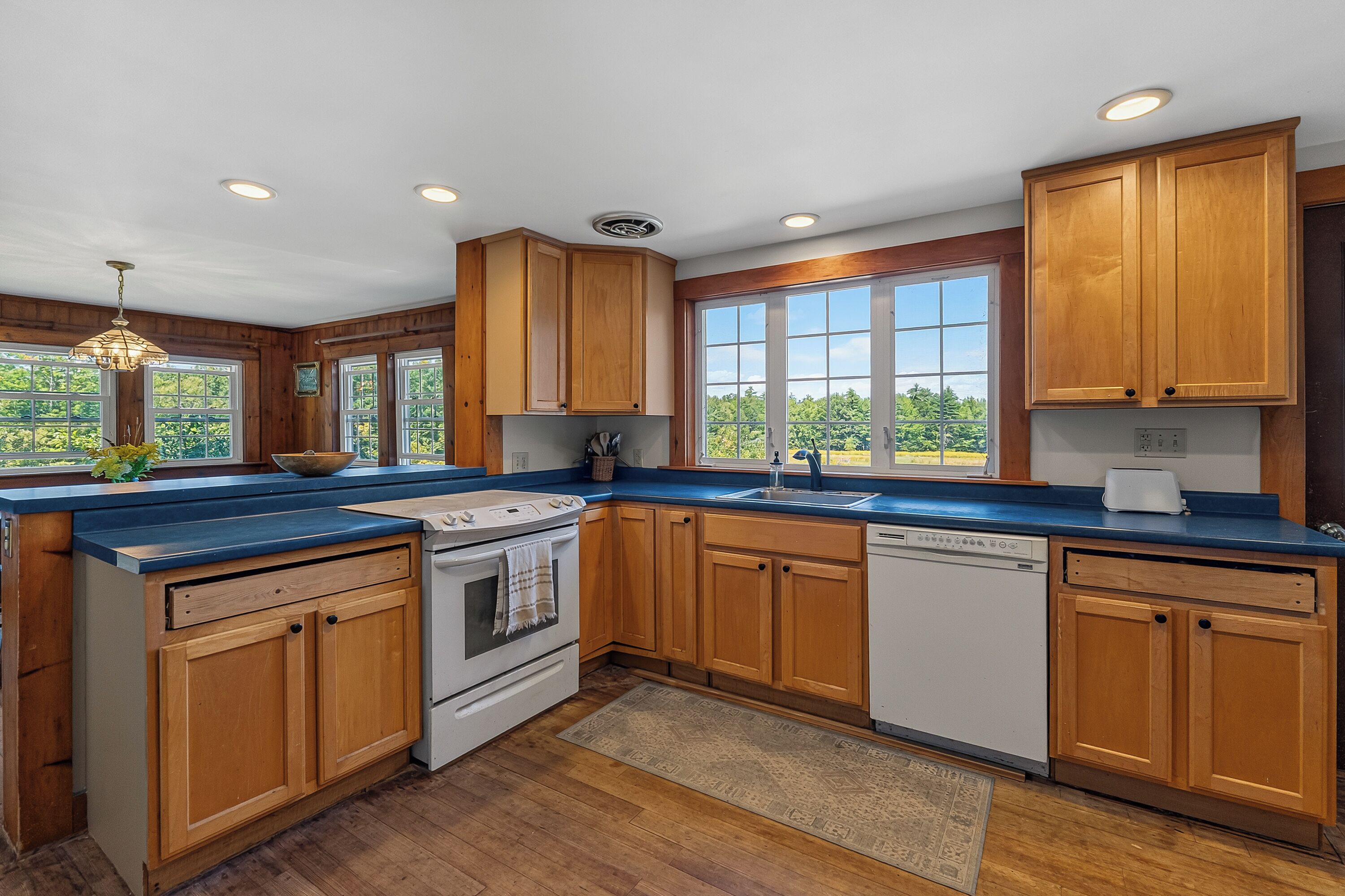 A modern kitchen with wooden cabinets, a central island, and a view of the outdoors.