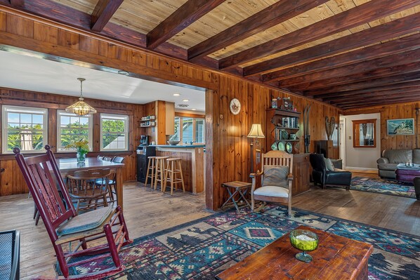 A spacious living area with a wooden ceiling, a dining table with chairs, a sofa, and a coffee table.