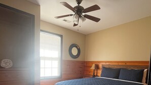 Ein Schlafzimmer mit Bett, Deckenventilator, Fenster mit Jalousien und einem hölzernen Kopfteil.