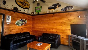 Ein Wohnzimmer mit Holzwand, zwei schwarzen Ledersofas, einem Holztisch, einem Deckenventilator und einem Fernseher auf einem Holzboden.
