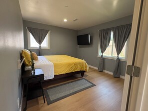 A bedroom with a bed, a desk, a chair, a TV, and two windows with curtains. - New Spacious 3-bedroom house in Beautiful Alhambra (Alhambra)