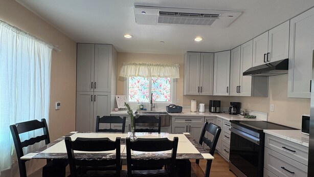 A compact kitchen with white cabinets, a dining table with chairs, and a window with floral curtains. - New Spacious 3-bedroom house in Beautiful Alhambra (Alhambra)