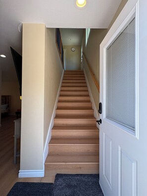 Eine Treppe führt zu einer zweiten Etage, rechts eine Tür und links eine an der Wand befestigte Uhr.