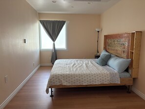 Ein Schlafzimmer mit einem hölzernen Bett, einem Nachttisch, einer Lampe und einem Fenster mit Vorhängen.