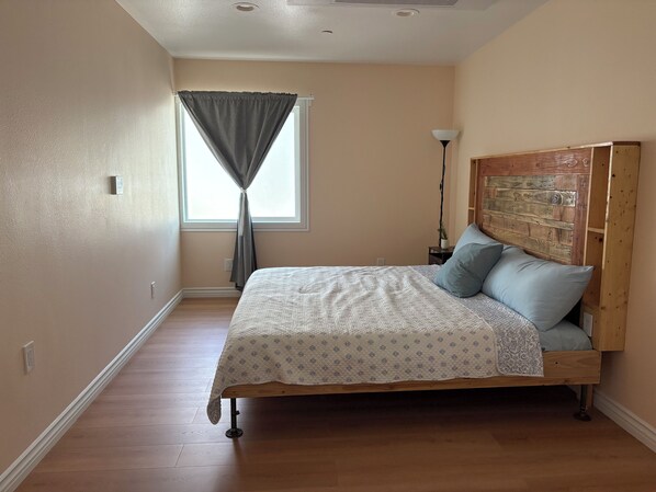 A bedroom with a wooden bed, a nightstand, a lamp, and a window with curtains. - New Spacious 3-bedroom house in Beautiful Alhambra (Alhambra)