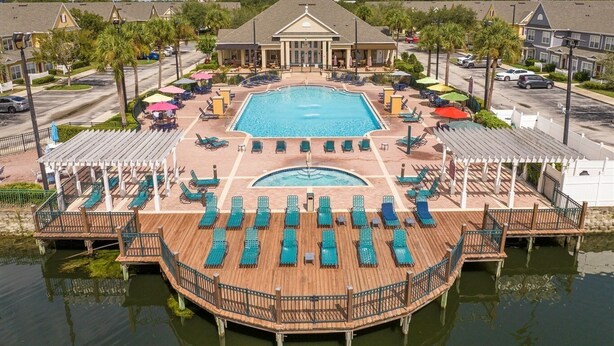 A hotel with a large central pool, multiple deck areas with sun loungers, and a view of the surrounding neighborhood.