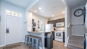 A modern kitchen with a central island, bar stools, a trash can, and a microwave.