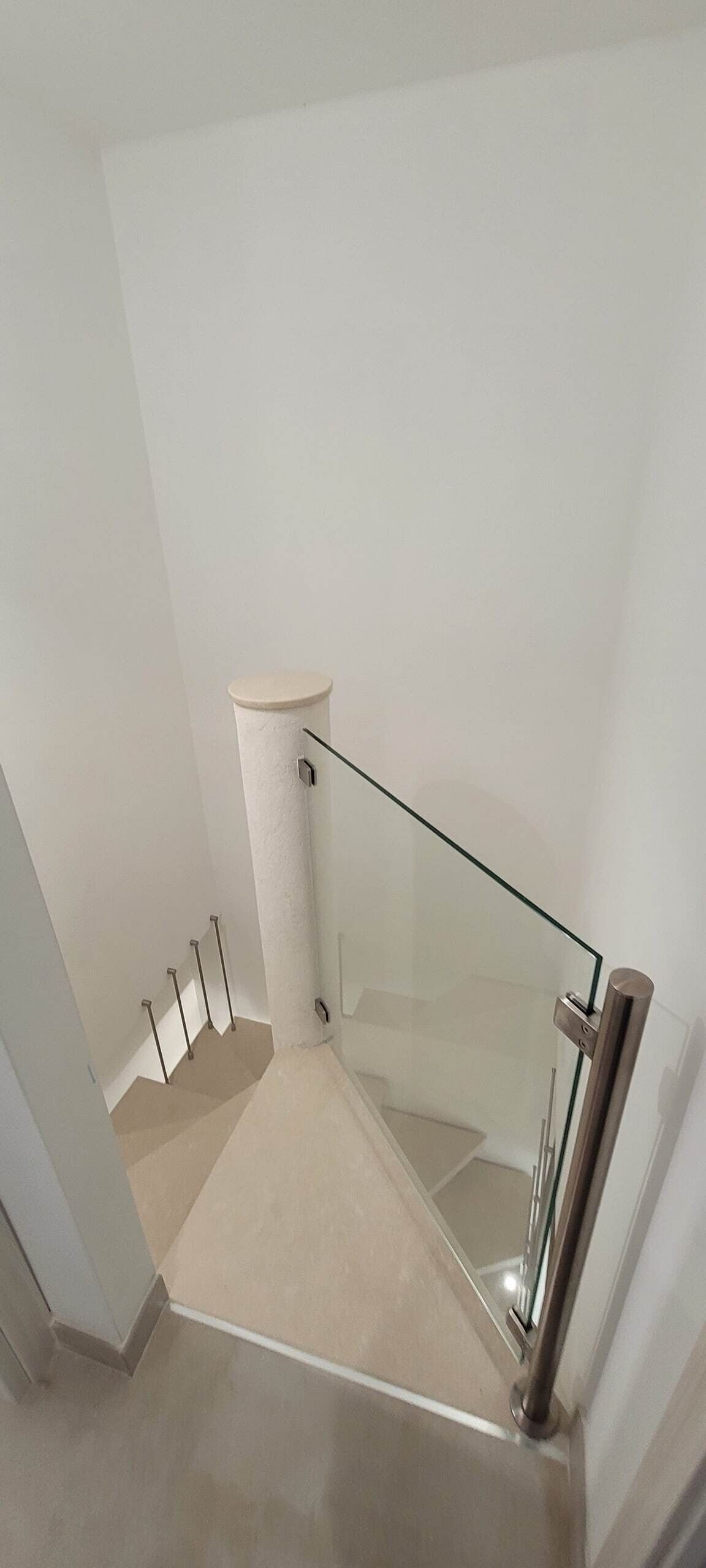 A modern staircase with a glass railing and a beige floor.
