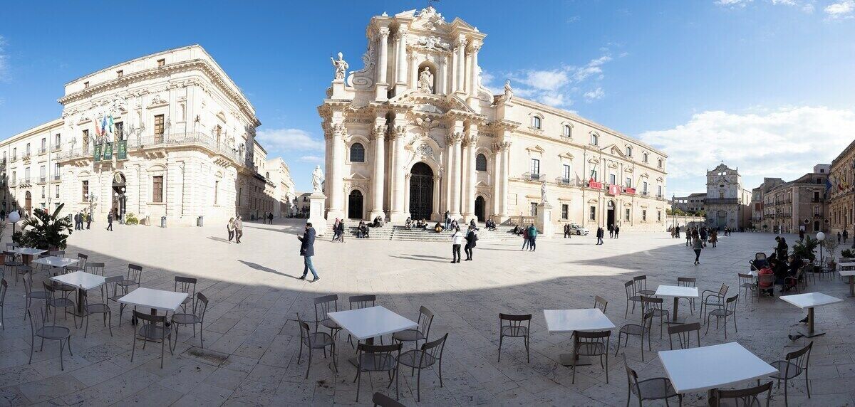 A spacious square with a prominent historical building featuring ornate architecture and a large central doorway.