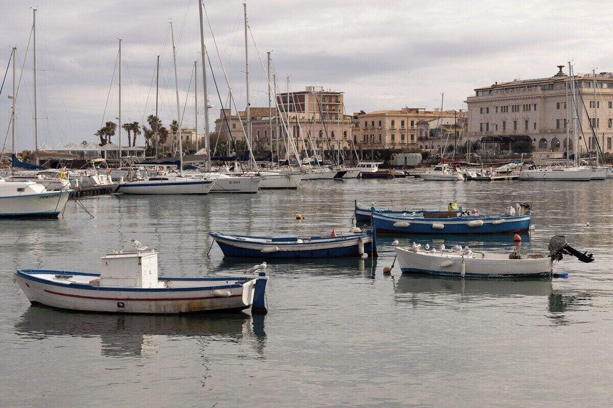 Un port de plaisance avec plusieurs bateaux amarrés, un bâtiment en arrière-plan et une eau calme.