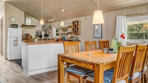 Eine moderne Küche mit Holzschränken, einer zentralen Kochinsel, Pendelleuchten und einem Essbereich mit Holztischen und einem Tisch.