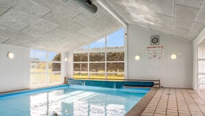 Ein Innenpool mit großen Fenstern, Fliesenboden und einer Sitzbank am Rand.