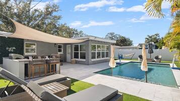 Ein Garten mit Pool, Sitzgelegenheiten im Freien und einer überdachten Terrasse.