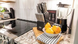 Une cuisine dotée d’une plaque de cuisson à induction noire, d’un ensemble de couteaux, d’un mixeur et d’un saladier rempli de citrons, le tout posé sur un plan de travail en marbre.