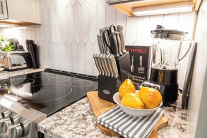 Una cocina con tope de inducción negro, un juego de cuchillos, una licuadora y un bol de limones sobre una encimera de mármol.