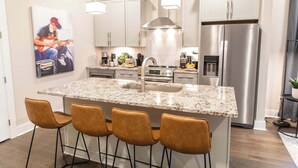 Une cuisine moderne dotée d’un comptoir en granit, d’appareils électroménagers en acier inoxydable et de quatre tabourets de bar.