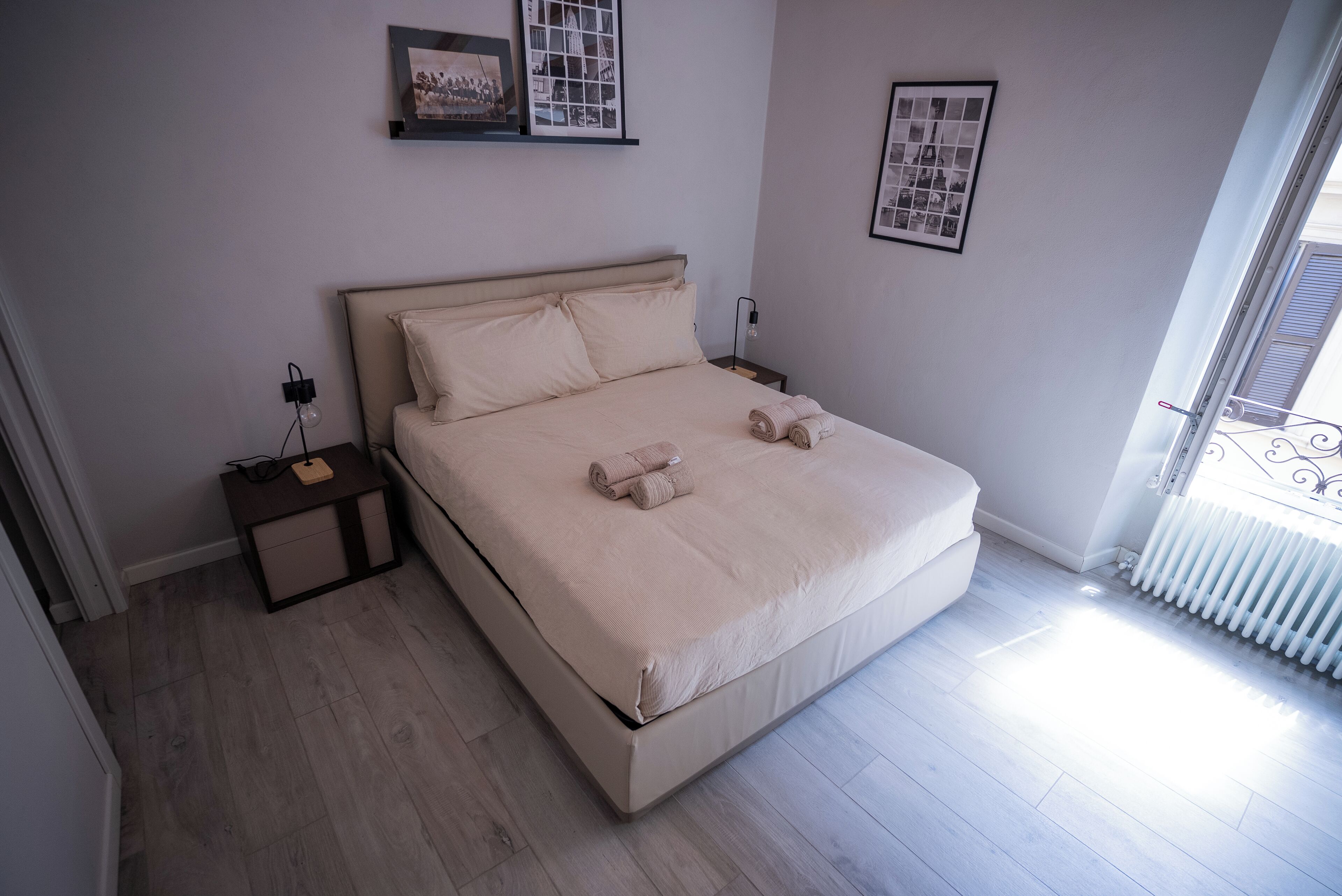 A bedroom with a bed, bedside tables, a radiator, and framed pictures on the walls.
