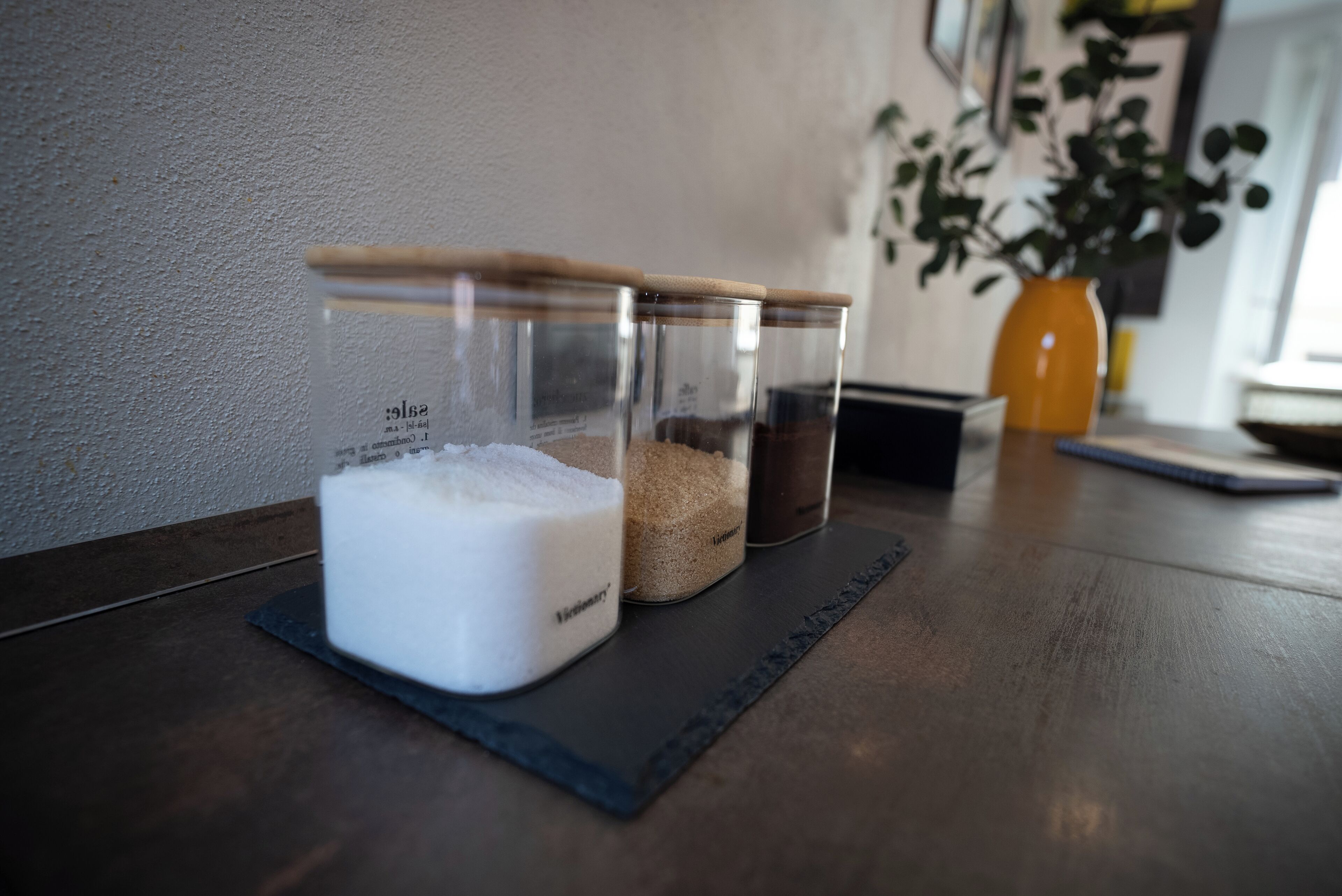 Tres recipientes de vidrio con tapas de madera sobre un tapete de pizarra oscura.
