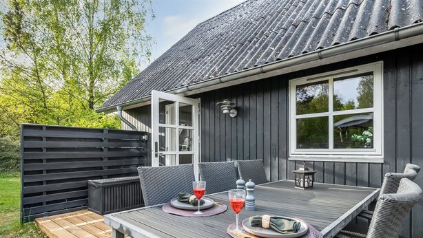 Eine Terrasse mit Tisch für zwei Personen, Sitzgelegenheiten im Freien und Blick auf das Haus.