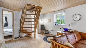 Ein modernes Wohnzimmer mit einer Holztreppe, einem Ledersofa, einem Esstisch und Blick ins Freie durch ein Fenster.