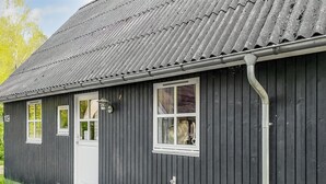 Ein dunkles Holzgebäude mit Metalldach, einer weißen Tür und drei Fenstern.