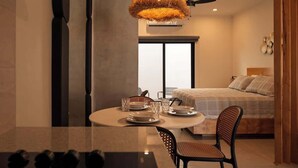 Ein modernes Schlafzimmer mit einem großen Bett, einer Essecke mit rundem Tisch und Blick auf die Stadt durch ein großes Fenster.