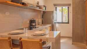 Una cucina compatta con isola centrale, due sedie in vimini, una macchina da caffè e un frigorifero.