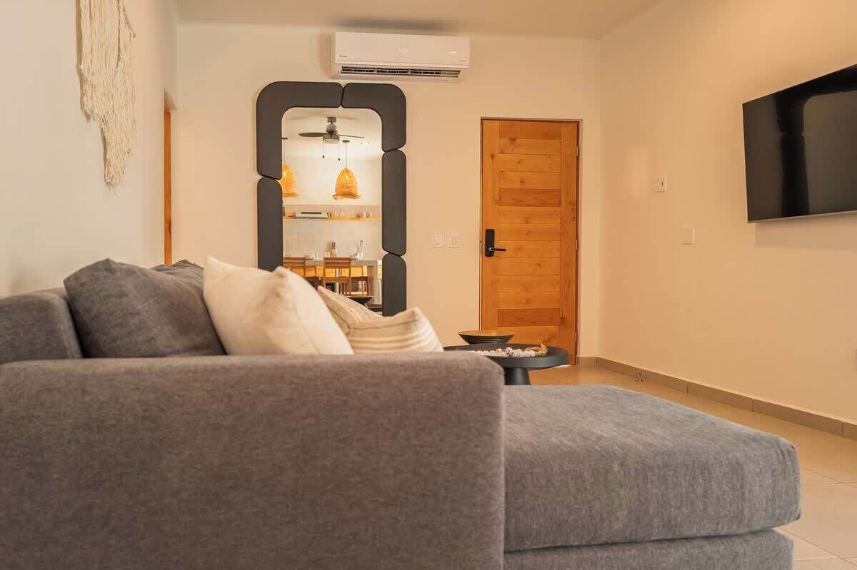 A modern living room with a grey sofa, a wooden door, and a mounted TV.