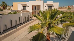 A modern residential building with a flat roof, white exterior walls, and a central courtyard with palm trees. - Palma 302 La Paz Downtown 2BR Suite Parking & Pool (La Paz)