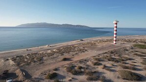 A coastal landscape with a lighthouse, sandy beach, and distant mountains. - Palma 302 La Paz Downtown 2BR Suite Parking & Pool (La Paz)
