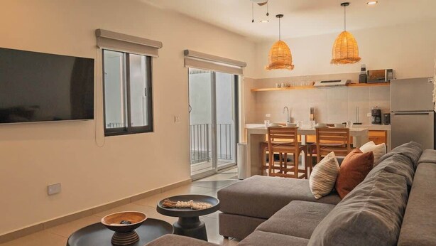 A modern living room with a sofa, a coffee table, and a TV. There is a kitchen area with a dining table and chairs. - Palma 302 La Paz Downtown 2BR Suite Parking & Pool (La Paz)