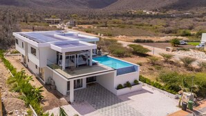 Et moderne hus med to etager, en swimmingpool, solpaneler og udsigt til de omkringliggende bakker.